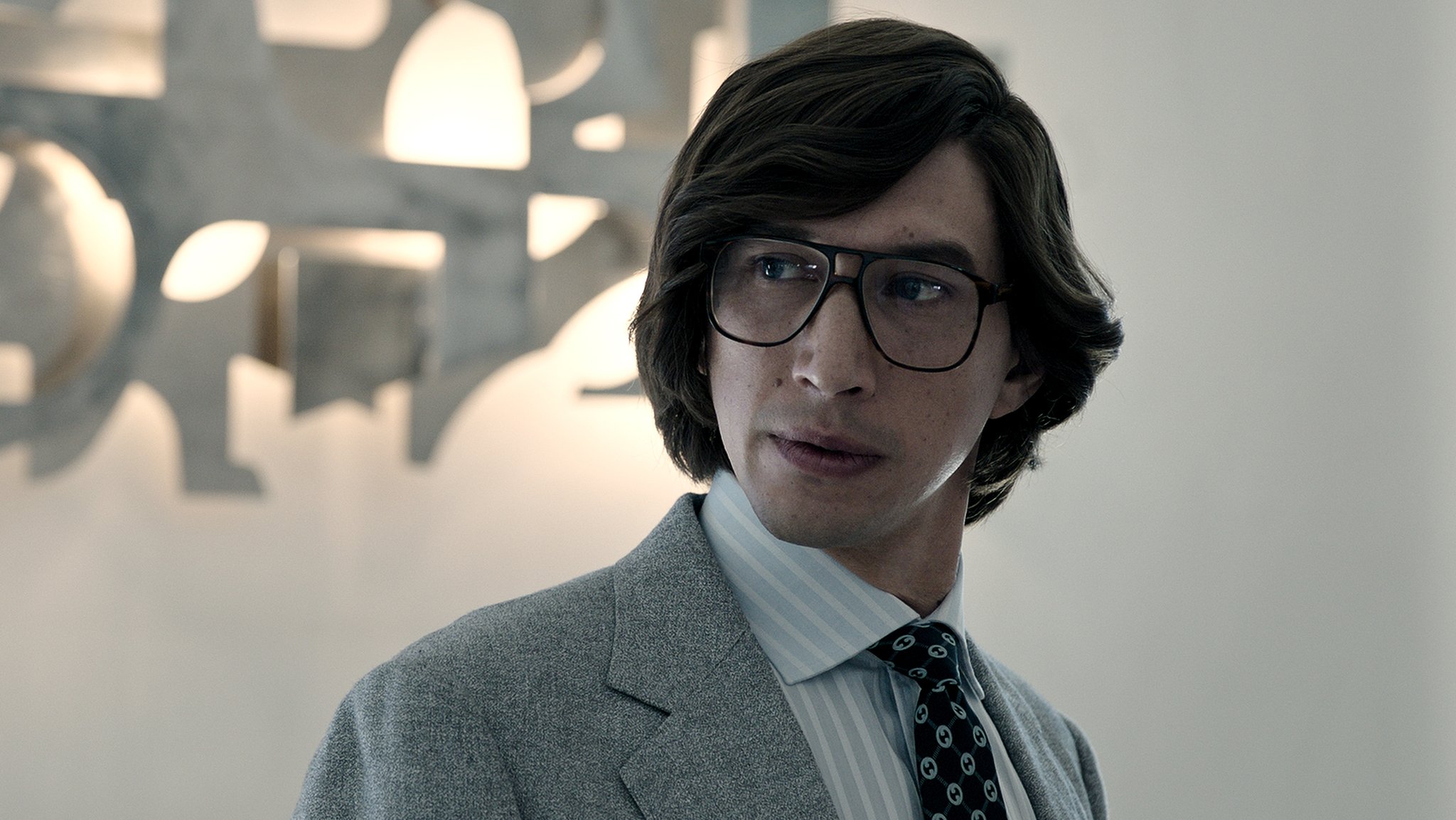 Adam Driver als junger Gucci mit halblangen Haaren und großer Brille