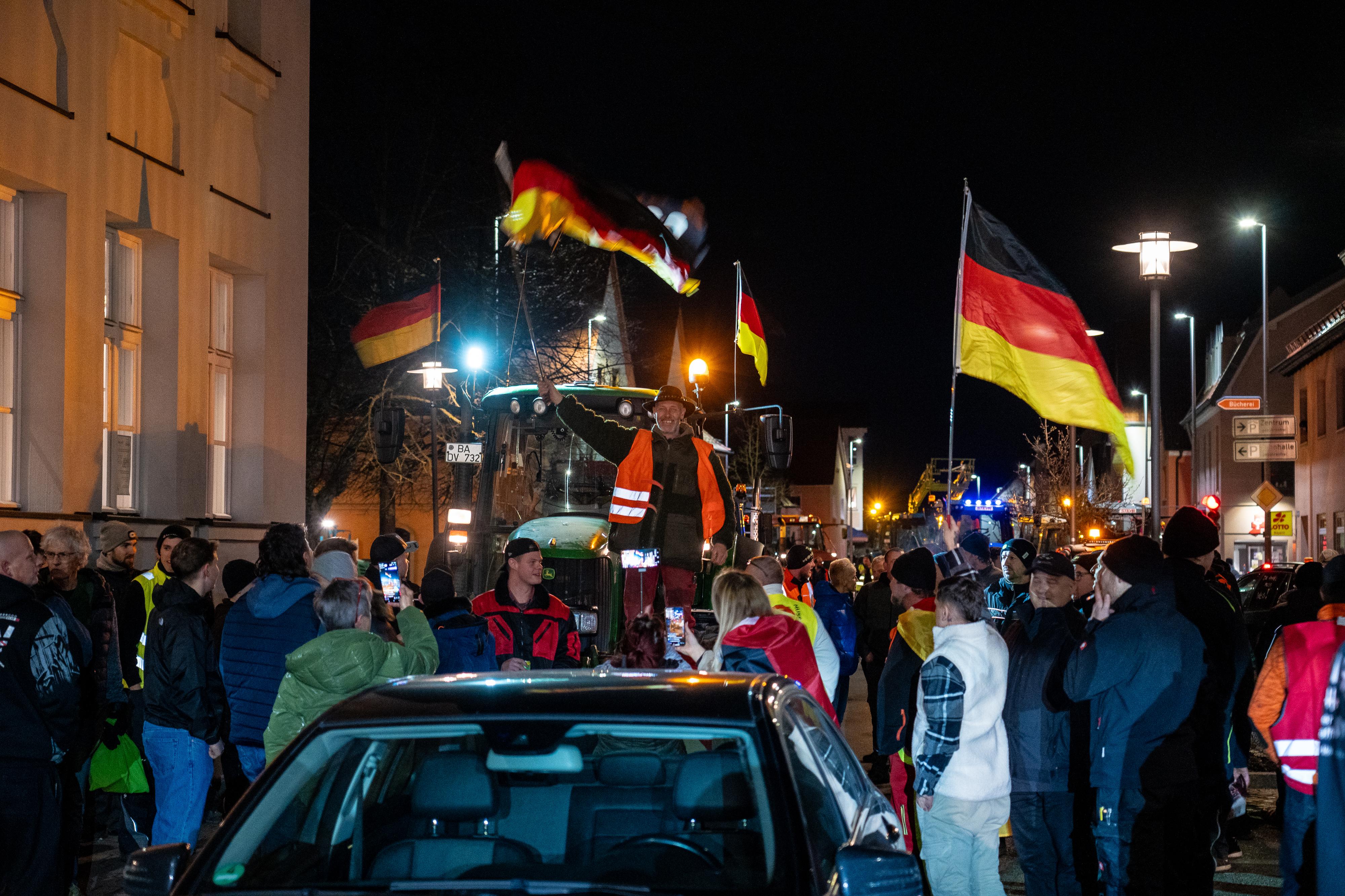 Menschen stehen auf der Straße und protestieren. Dabei sind auch Deutschlandfahnen und Traktoren zu sehen. 