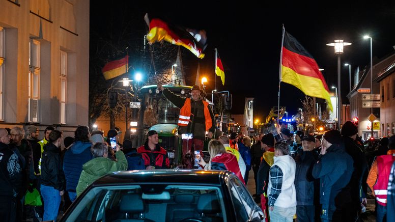 Menschen stehen auf der Straße und protestieren. Dabei sind auch Deutschlandfahnen und Traktoren zu sehen.  | Bild:News5/Merzbach