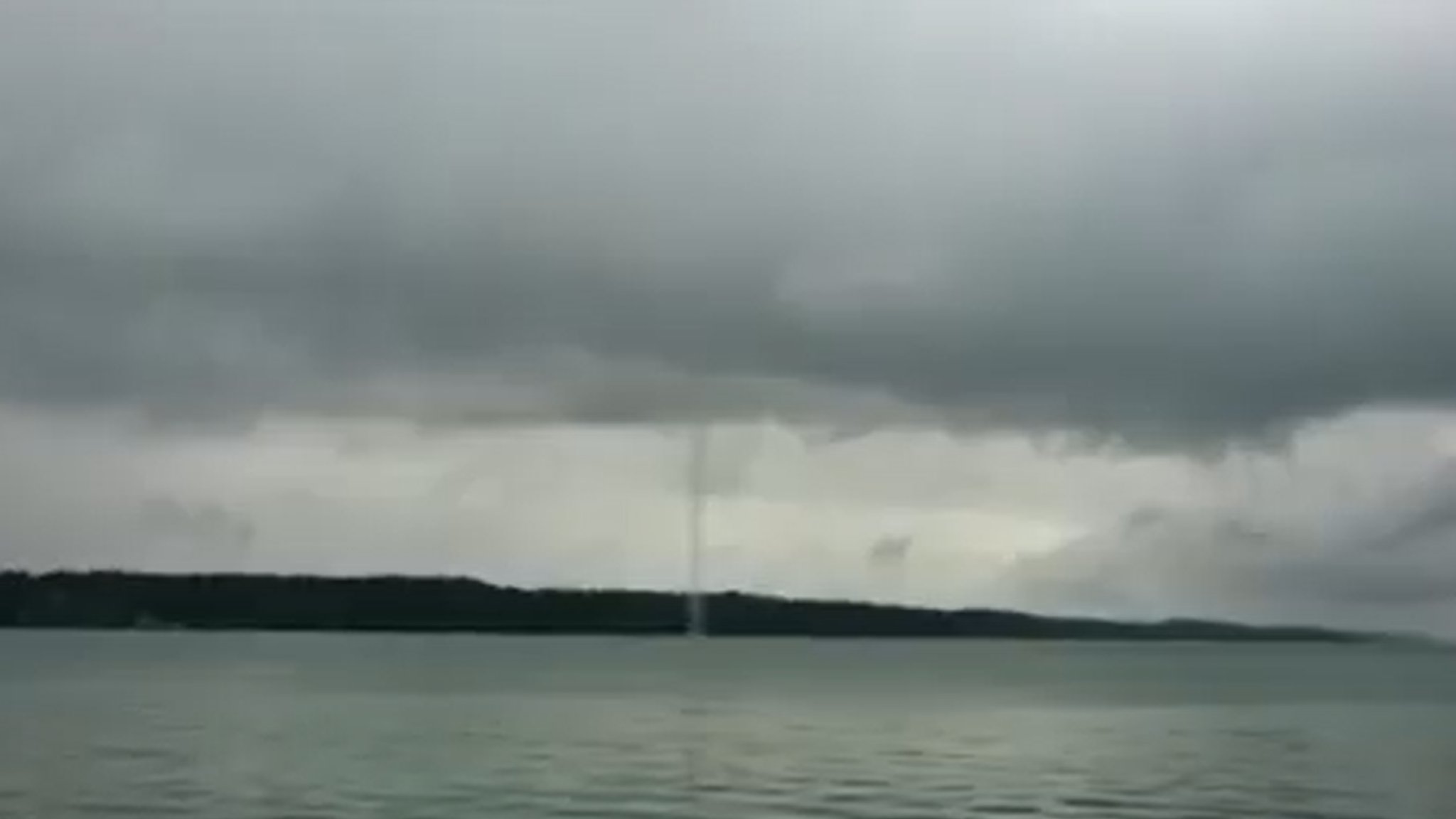 Eine Wetterhose zwischen Starnberger See und grauen Wolken darüber.