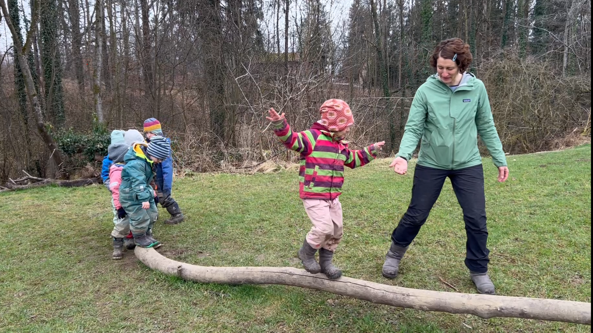 Die pädagogische Ergänzungskraft Simone Gobmeier hilft Kindergartenkindern beim Balancieren auf einem Baumstamm. 
