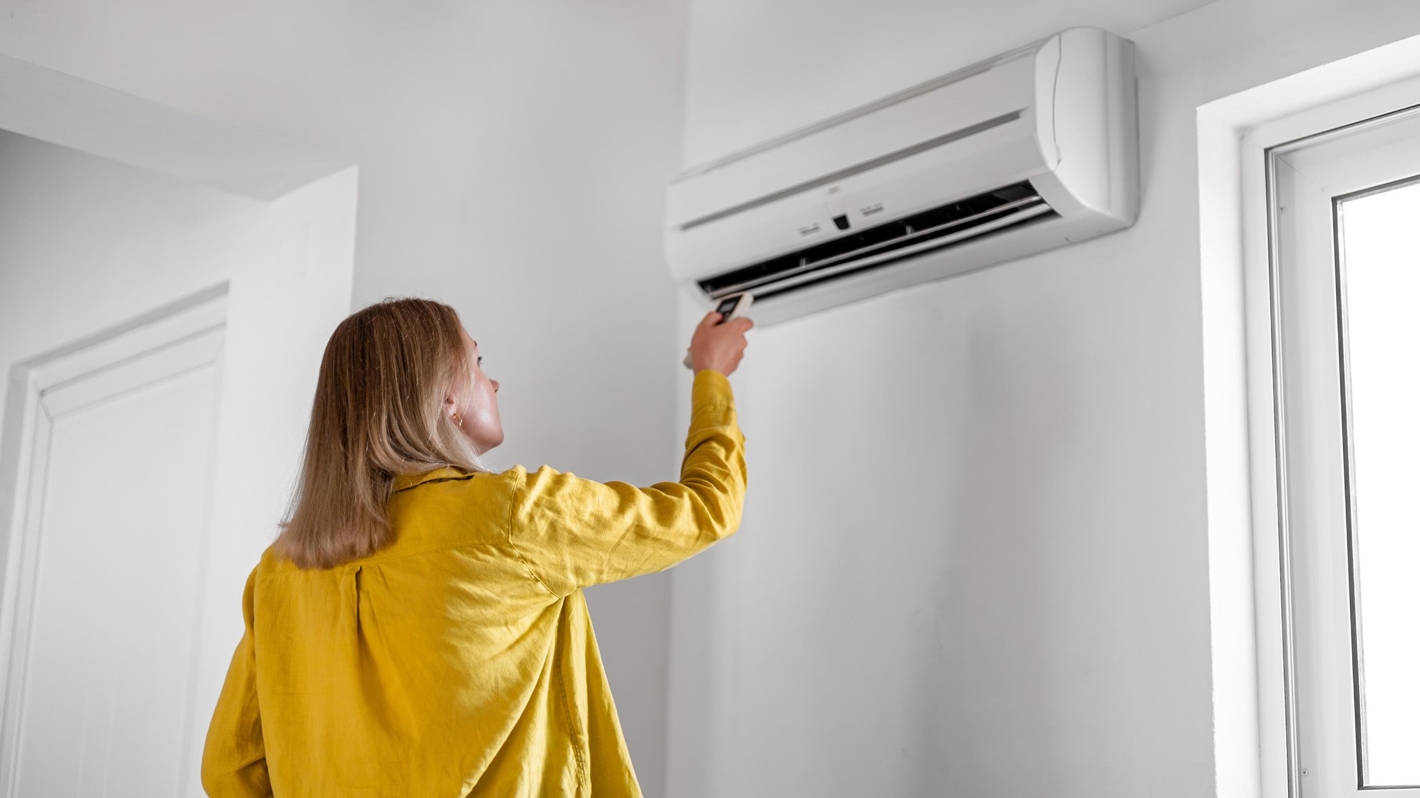 Eine Frau reguliert mit einer Fernbedienung die Klimaanlage.