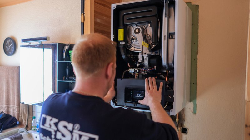 Der Mitarbeiter einer Sanitär- und Heizungsbaufirma installiert eine moderne Gasbrennwerttherme in einem Einfamilienhaus. 