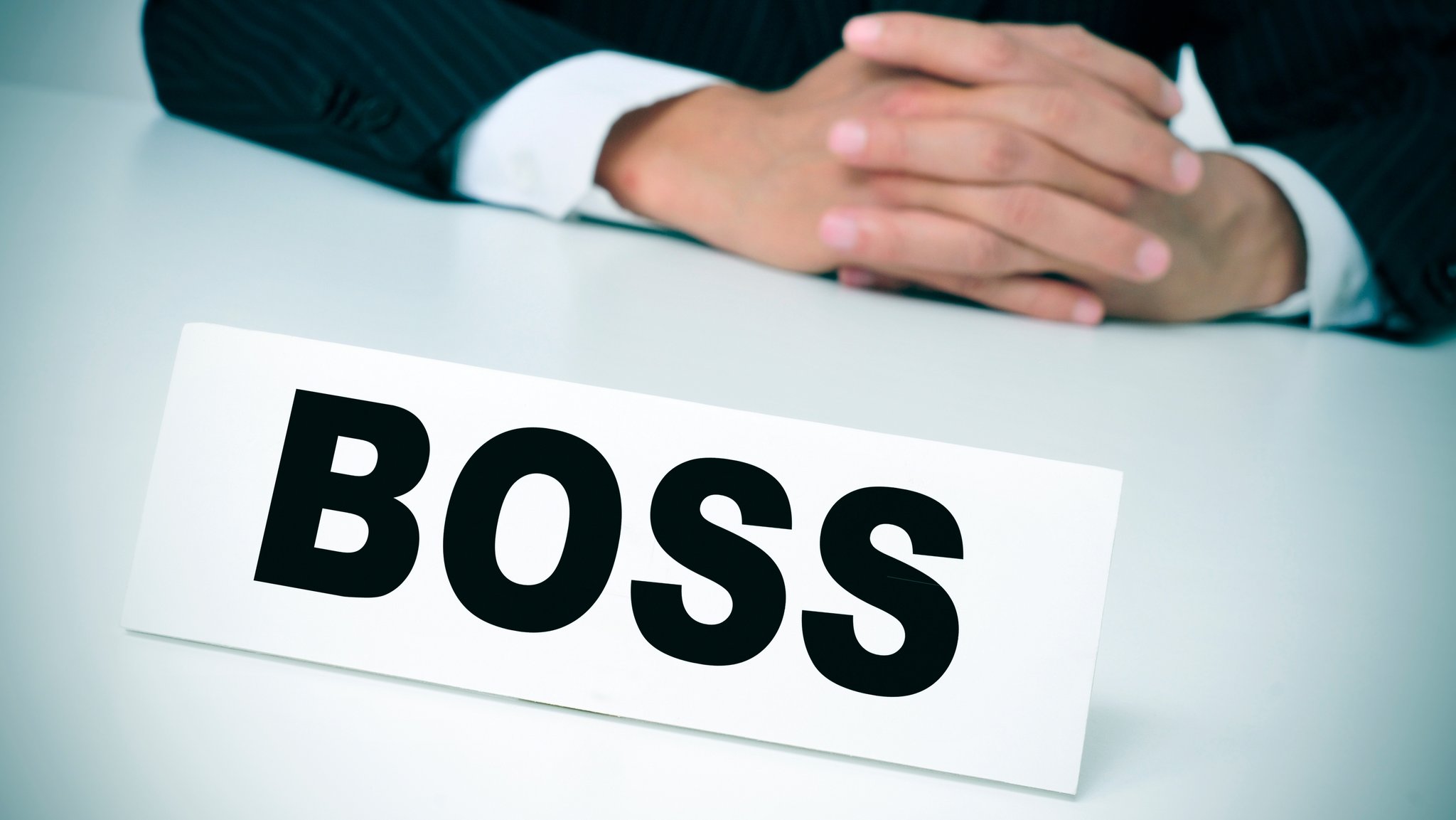 Mann im Anzug mit gefalteten Händen sitzt hinter einem Schild mit der Aufschrift "Boss" (Symbolbild) | Bild: colourbox.com Mann im Anzug mit gefalteten Händen sitzt hinter einem Schild mit der Aufschrift "Boss" (Symbolbild)