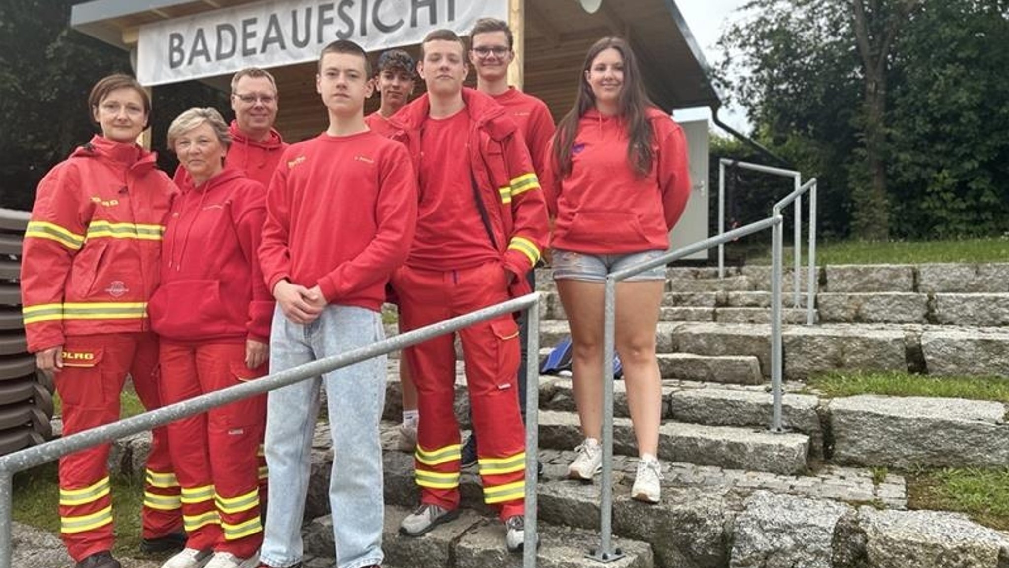 Eine Gruppe steht in roter Rettungskluft der DLRG auf einer Steintreppe.