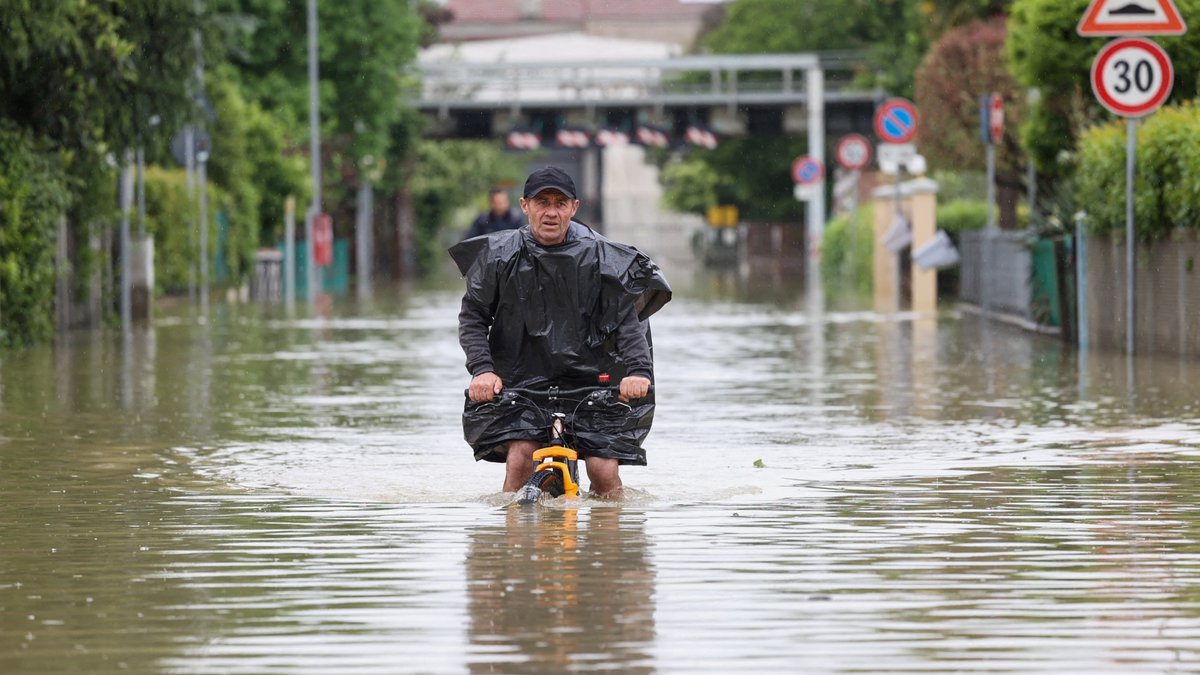 Ein Mann versucht sich mit dem Fahrrad auf einer überschwemmten Straße durchzuschlagen, Emilia Romagna, Italien.