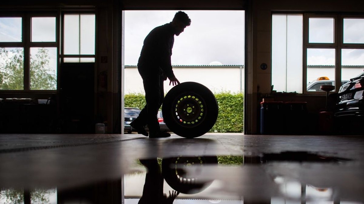 Ein Auszubildender zum Kfz-Mechatroniker rollt einen Reifen durch eine Werkstatt.
