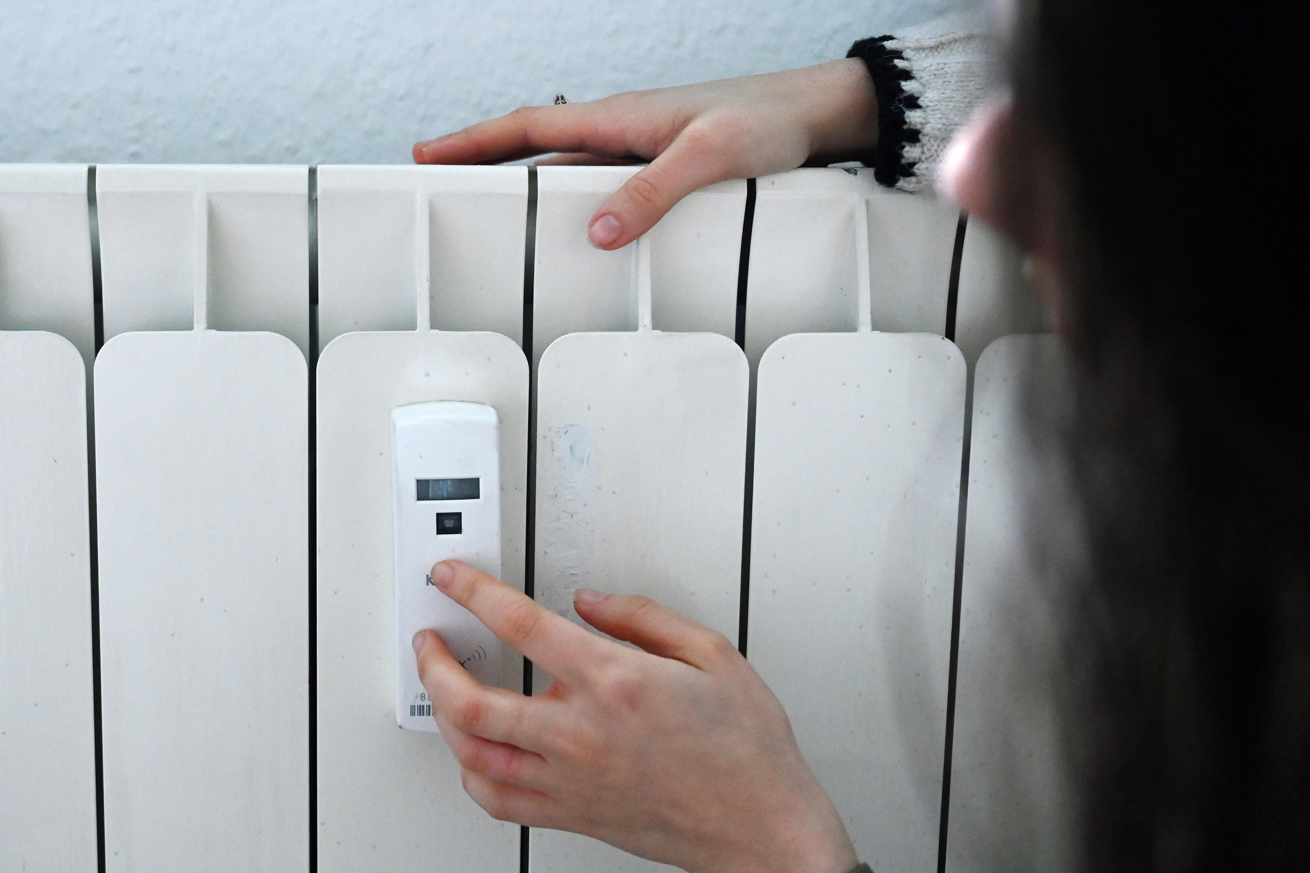 (Symbolbild): Eine Frau berührt einen Heizkörper in einer Wohnung, an dem ein Heizkostenverteiler angebracht ist.
