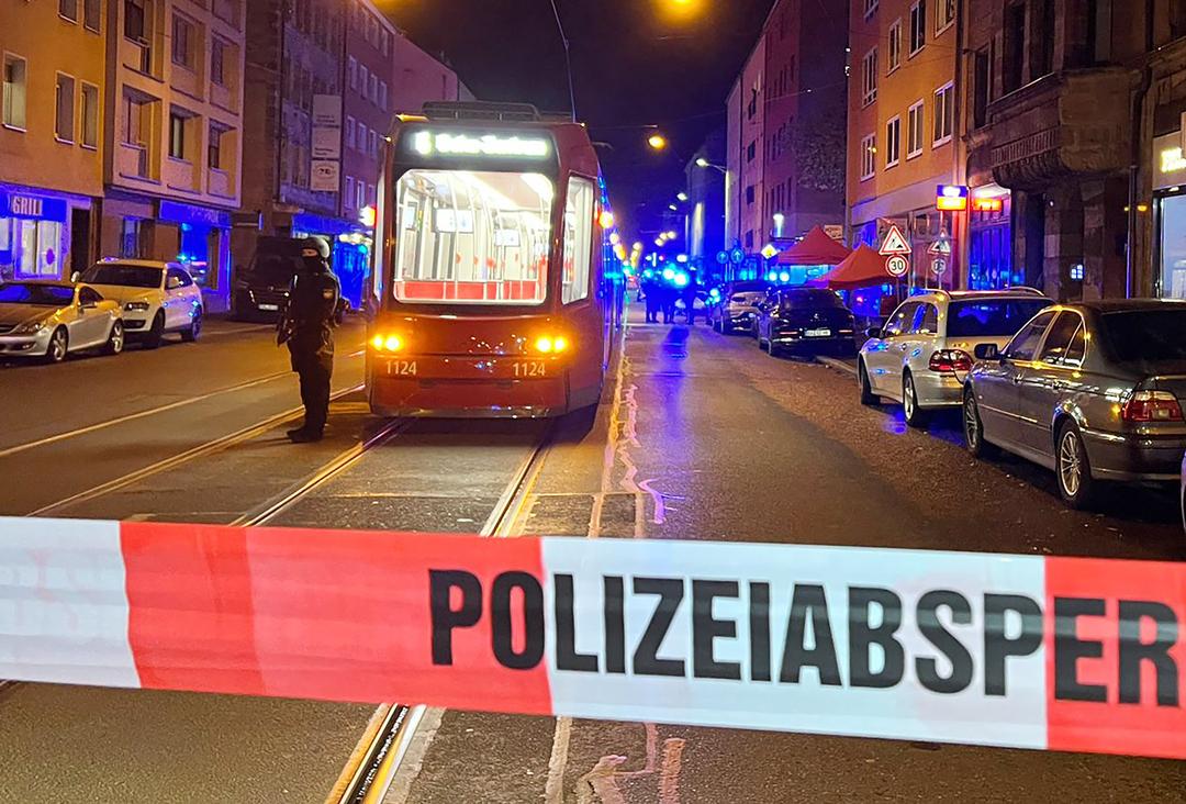 Ein Polizist steht mit einer Maschinenpistole neben einer Straßenbahn hinter einer Polizeiabsperrung.