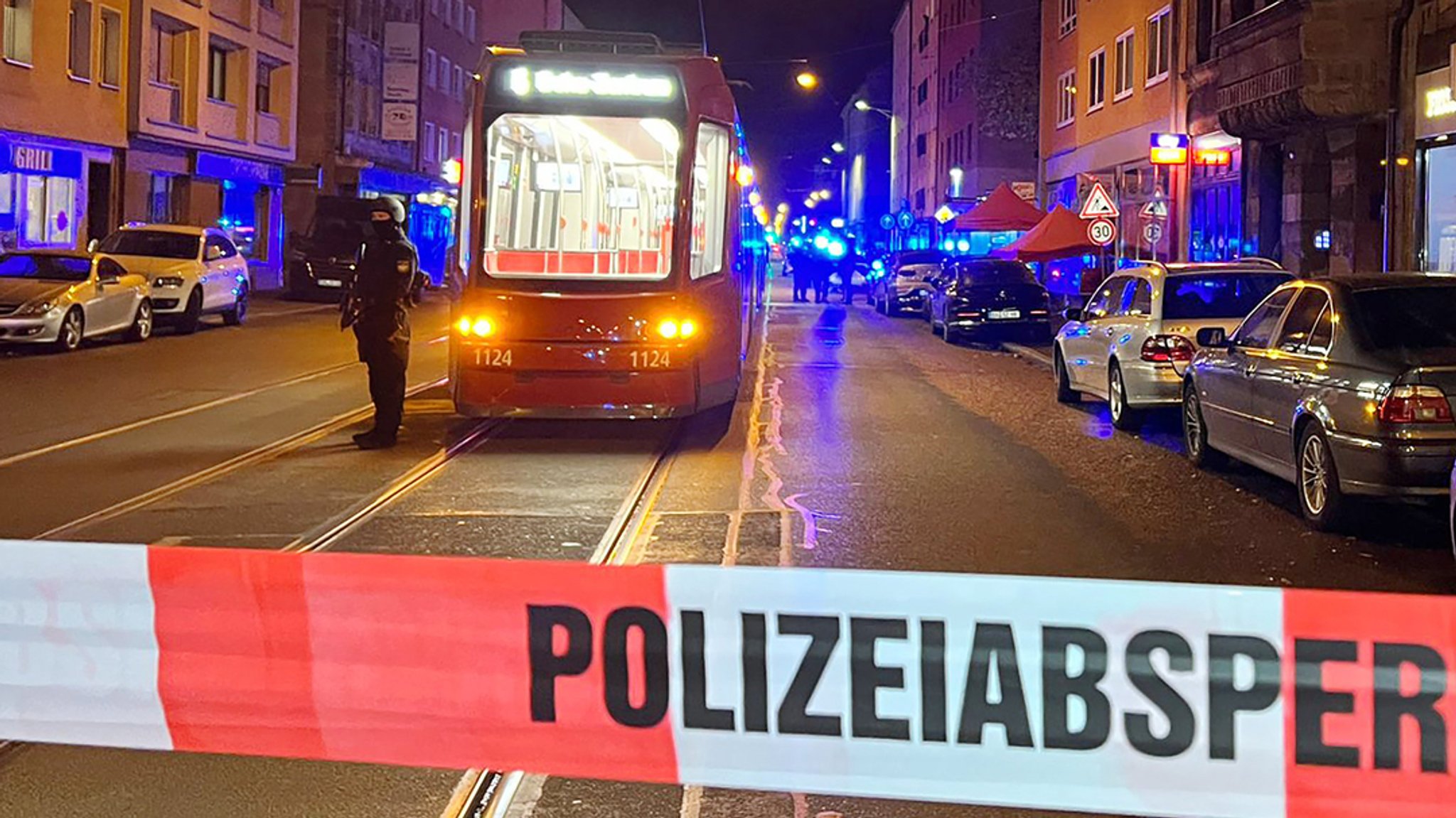 Ein Polizist steht mit einer Maschinenpistole neben einer Straßenbahn hinter einer Polizeiabsperrung.