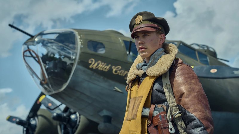 Austin Butler als junger US-Bomberpilot Buck Cleven. In brauner Lederjacke und mit Fallschirmausrüstung steht er vor einer  Reihe Jagdbomber. 