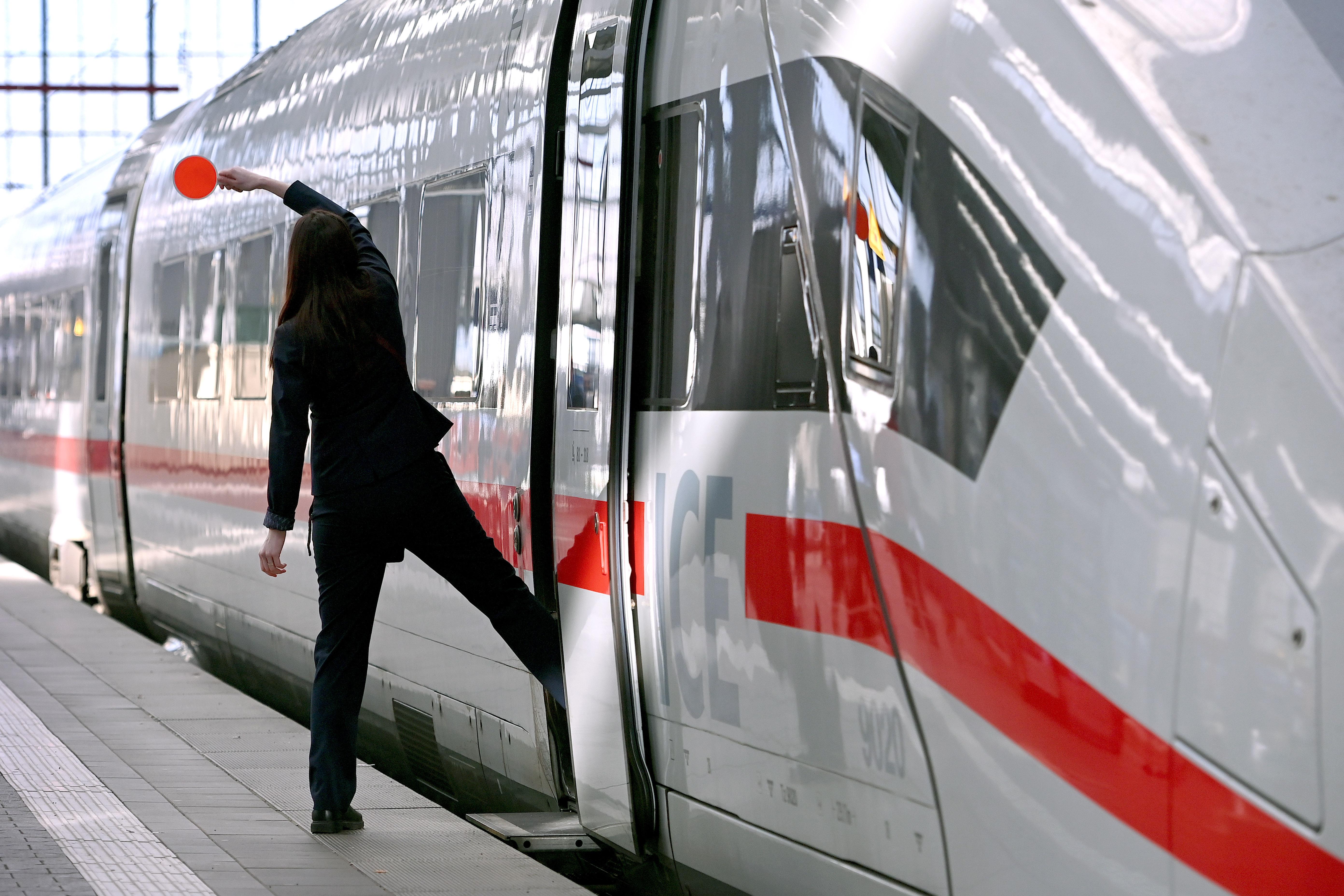 Eine Zugbegleiterin winkt vor der Abfahrt eines ICE mit der Kelle.