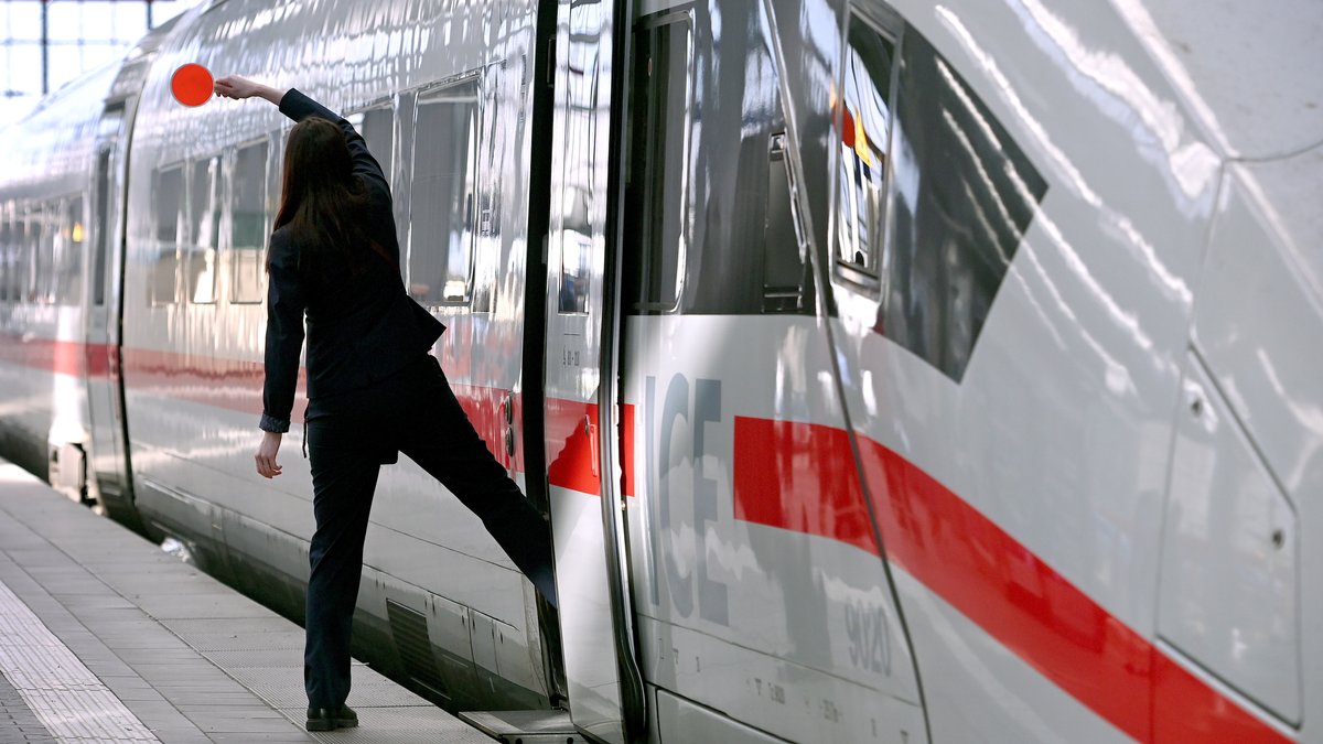 Eine Zugbegleiterin winkt vor der Abfahrt eines ICE mit der Kelle.