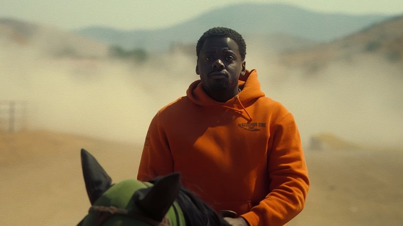 Filmbild aus "Nope": Daniel Kaluuya reitet im orangefarbenen Kapuzenpulli der Kamera entgegen