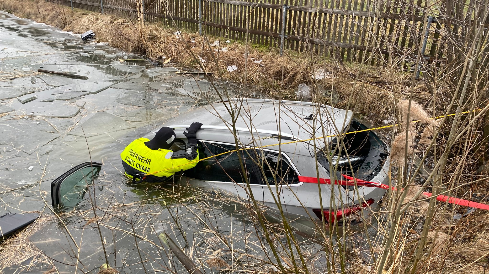 Ein Auto liegt im Wasser und ein Mann der Feuerwehr der Stadt Cham steht im Wasser neben dem Auto.