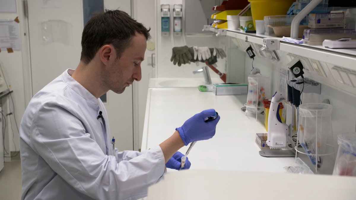 Ein Mann im weißen Kittel bei der Arbeit mit einer Pipette und Gummihandschuhen. | Bild: BR Ein Mann im weißen Kittel bei der Arbeit mit einer Pipette und Gummihandschuhen.