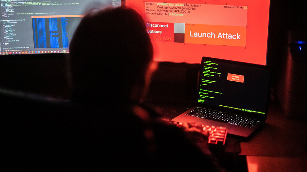 Ein Mann sitzt vor Bildschirmen, die Hacker-Programme und eine fiktive Fernlösch-Software zeigen.
