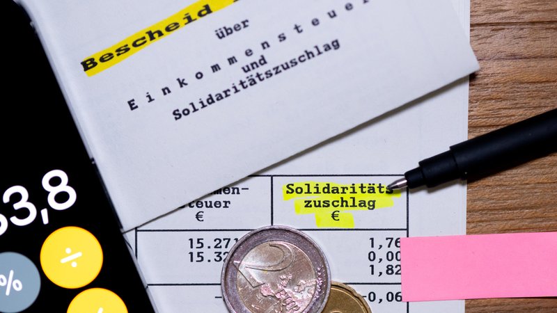Münzen liegn auf einem Einkommenssteuerbescheid, der auch den Solidaritätszuschlag enthält | Bild: dpa-Bildfunk/Sven Hoppe Münzen liegn auf einem Einkommenssteuerbescheid, der auch den Solidaritätszuschlag enthält