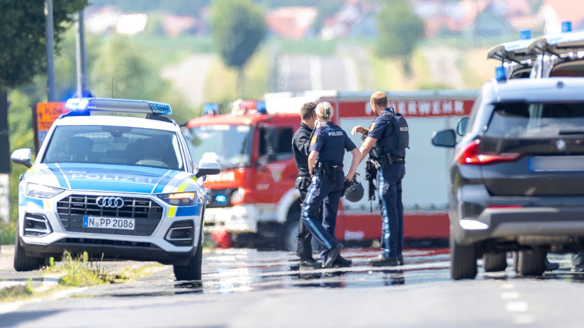 Polizei, Feuerwehr und das SEK stehen beim Einsatz in Uffenheim an einer Asylunterkunft auf einer Straße.