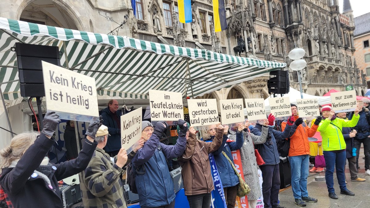 Menschen halten vor dem Münchner Marienplatz Plakate mit Anti-Kriegs-Parolen hoch.