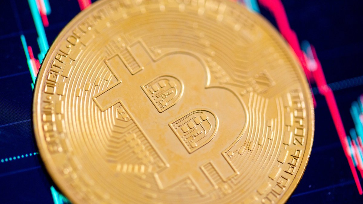 Eine Bitcoin-Münze liegt auf einem Bildschirm, der den Bitcoin - US-Dollar Kurs zeigt. 