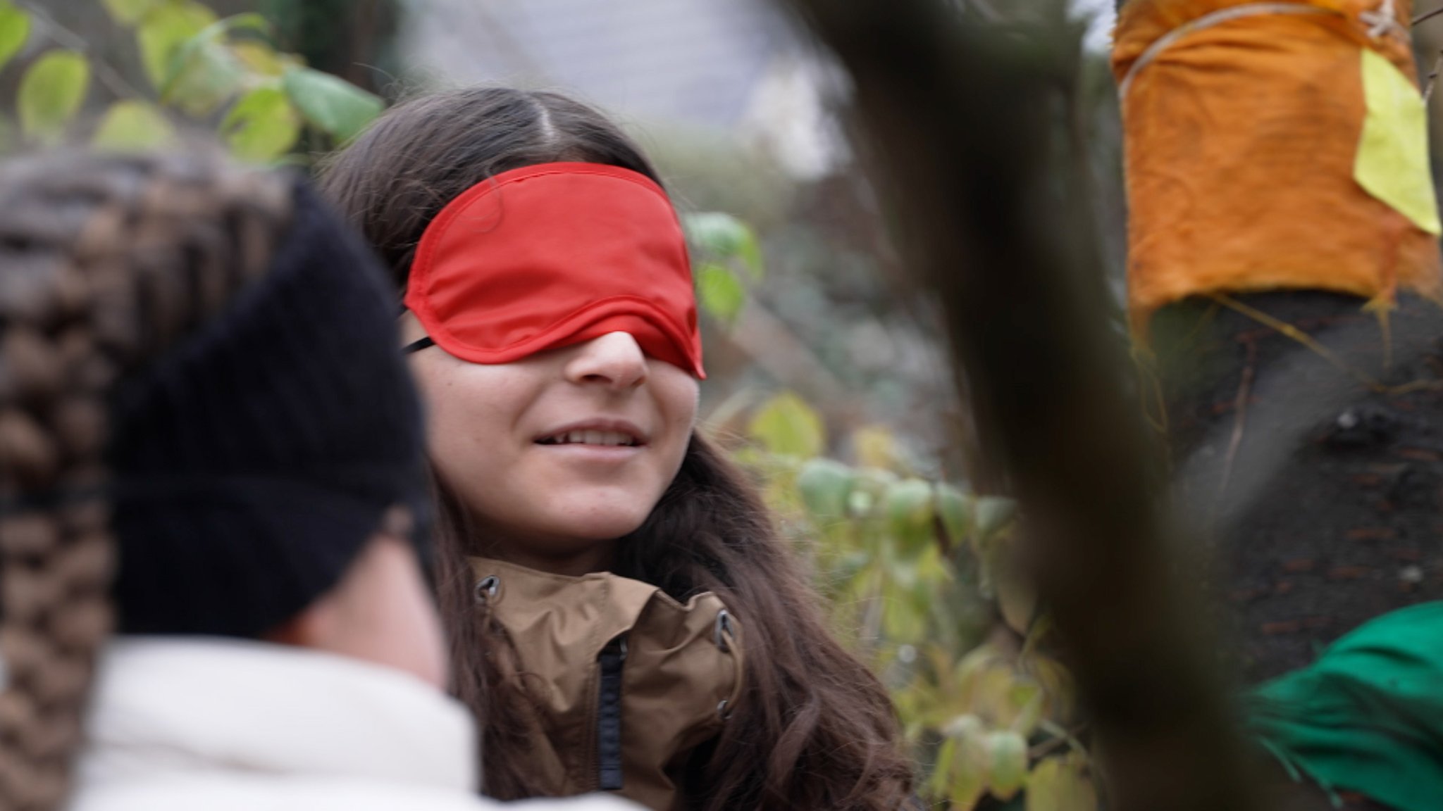 Nahaufnahme einer Schülerin im Wald, die eine rote Stoffmaske über den Augen trägt