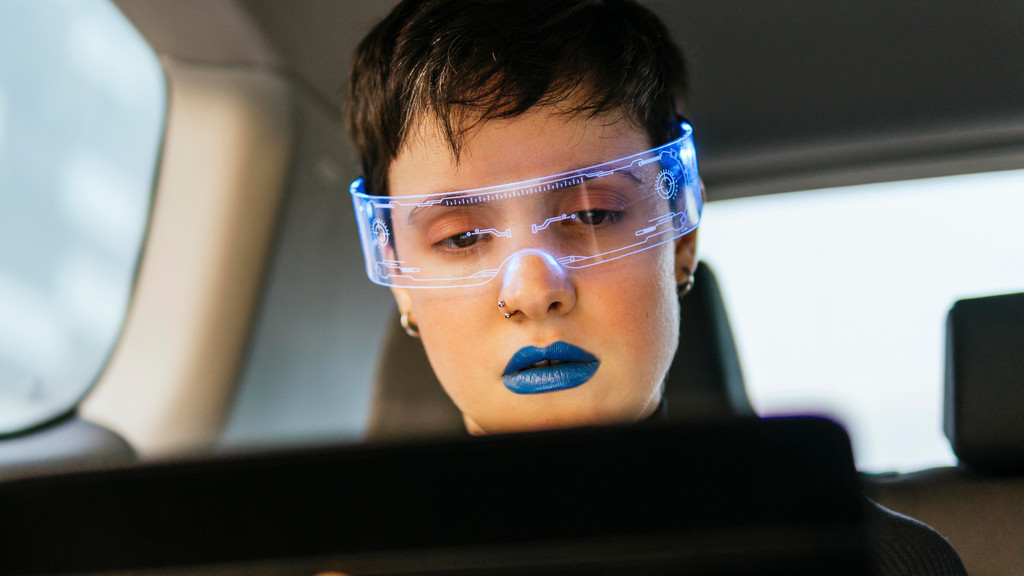 Konzeptstudie: Eine Frau sitzt mit Smart-Brille und Tablet-Computer am Steuer eines Autos