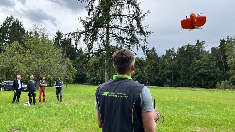Ein Mann lässt eine rote Drohne am Waldrand steigen | Bild: BR/Margit Ringer Ein Mann lässt eine rote Drohne am Waldrand steigen