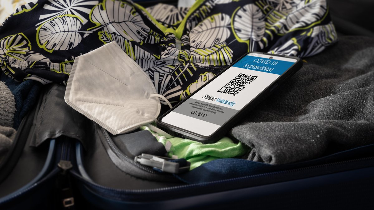 Ein Smartphone, das auf einer Reisetasche liegt, mit einem Covid-19-Impfzertifikat