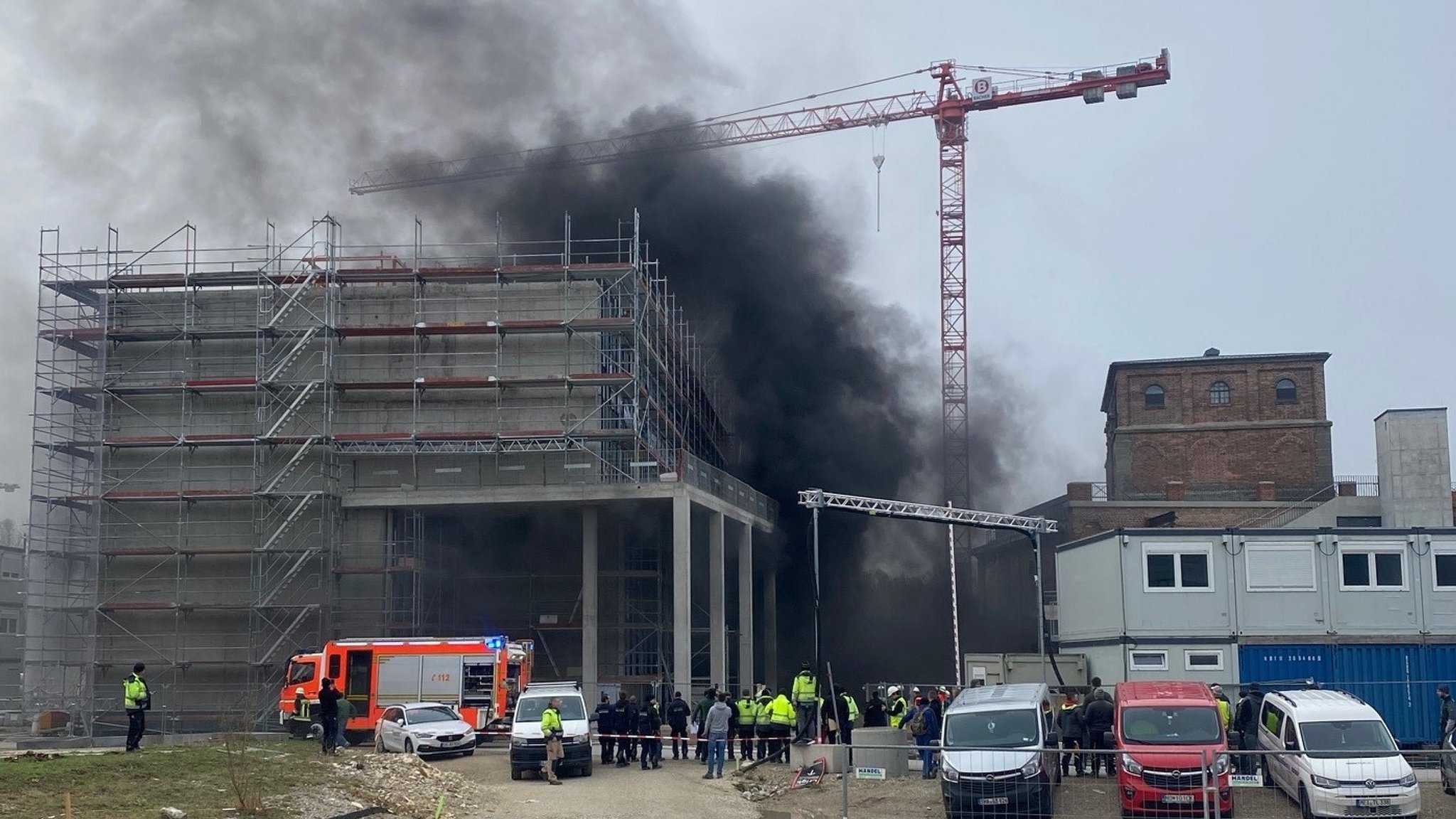 Die Baustelle für das Digitale Gründerzentrum Ingolstadt. Ein eingerüsteter Rohbau, darüber steigt dicker schwarzer Rauch auf. Vor dem Robhau stehen viele Menschen und ein Feuerwehrauto.