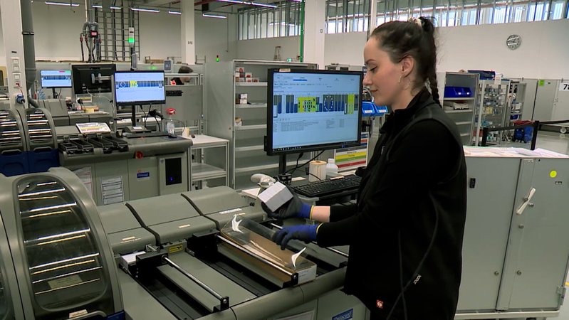 Eine Mitarbeiterin des Chip-Karten-Herstellers legt Karten-Rohlinge in eine Maschine ein.