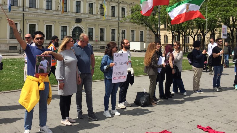 Demonstrierende stehen an der Münchner Ludwigstraße und halten Iran-Flaggen, Fotos und Plakate in die Höhe.
