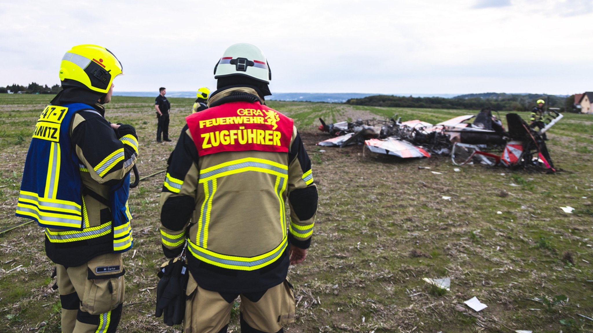 Einsatzkräfte der Feuerwehr Gera stehen an der Unglücksstelle, an der zwei Kunstflieger kollidiert und abgestürzt sind. 