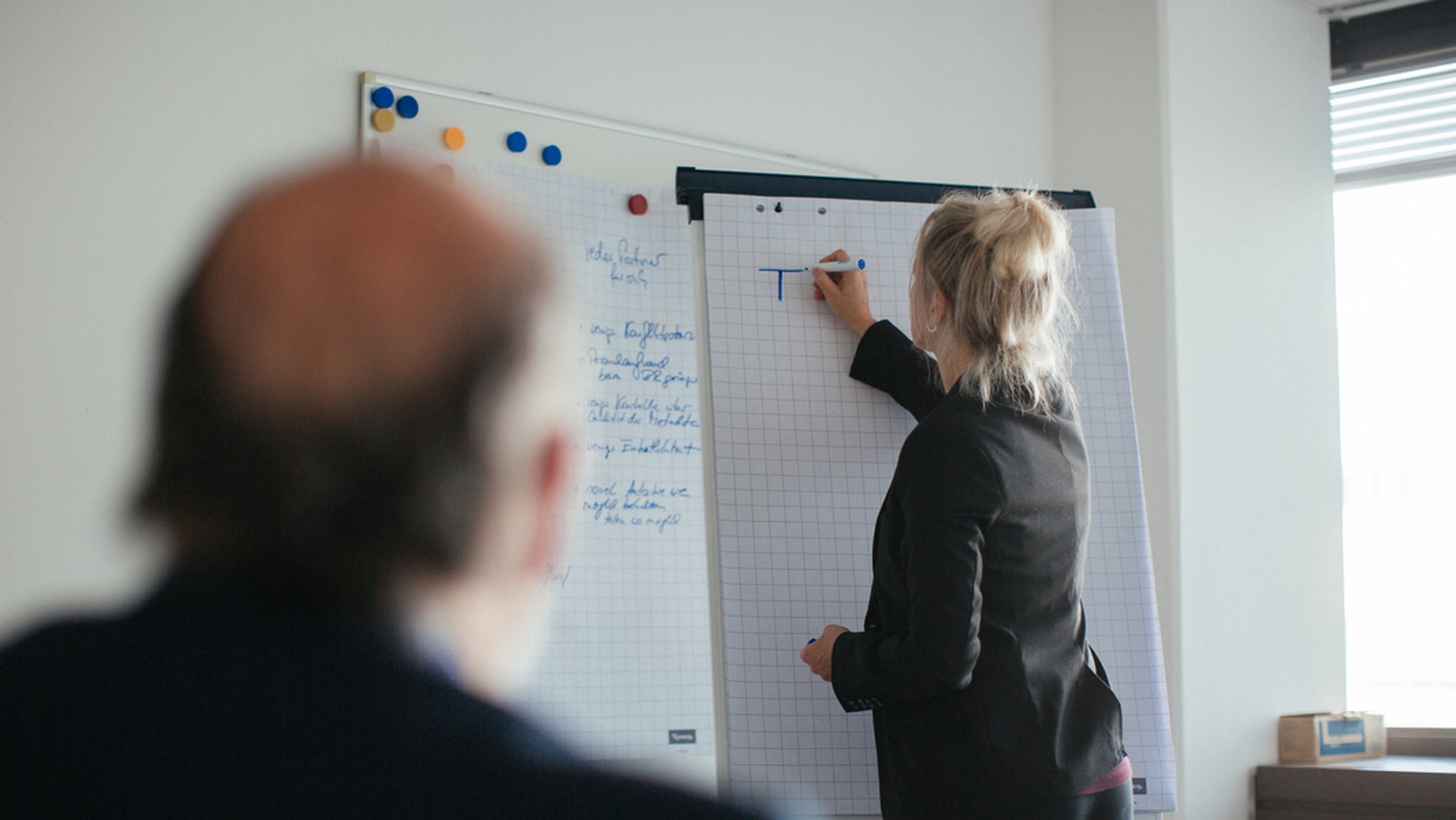 Eine Frau und ein Kollege besprechen etwas an einem Flipchart in einem Büro