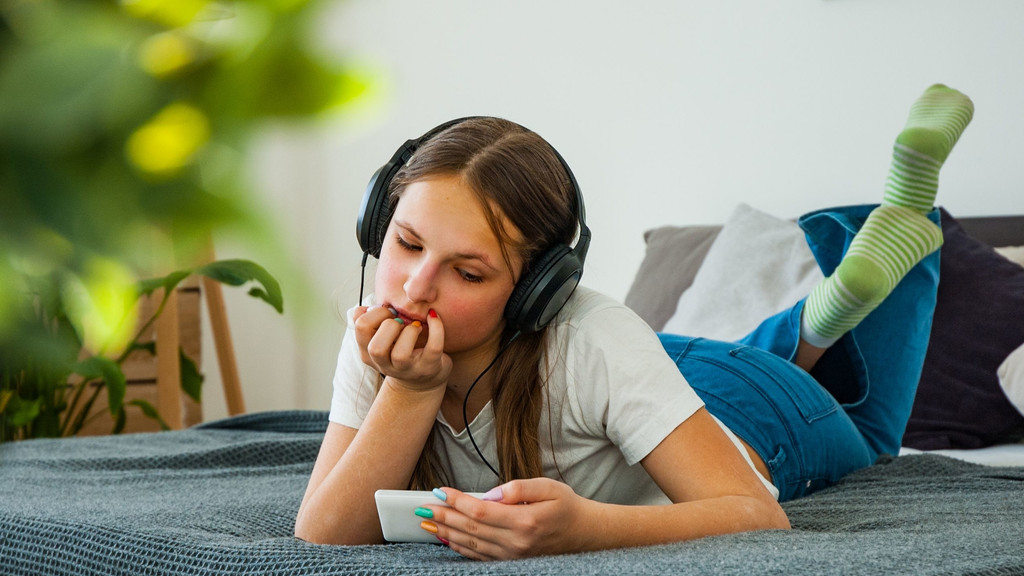 Mädchen liegt auf dem Bett und hört über Kopfhörer Inhalte vom Smartphone