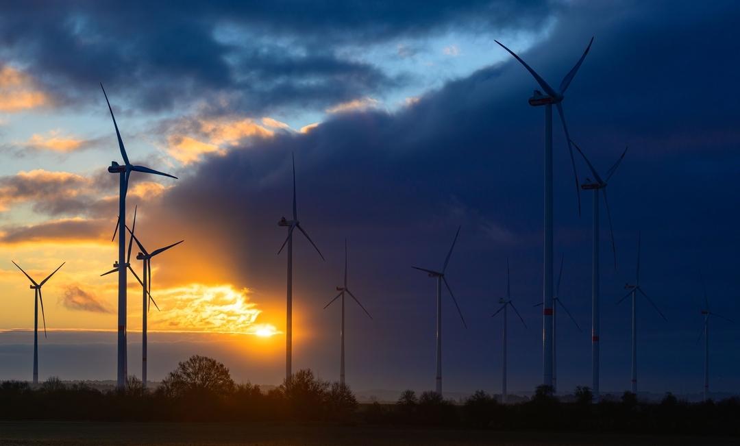 Windräder bei Sonnenaufgang mit dunklen Wolken (Symbolbild).
