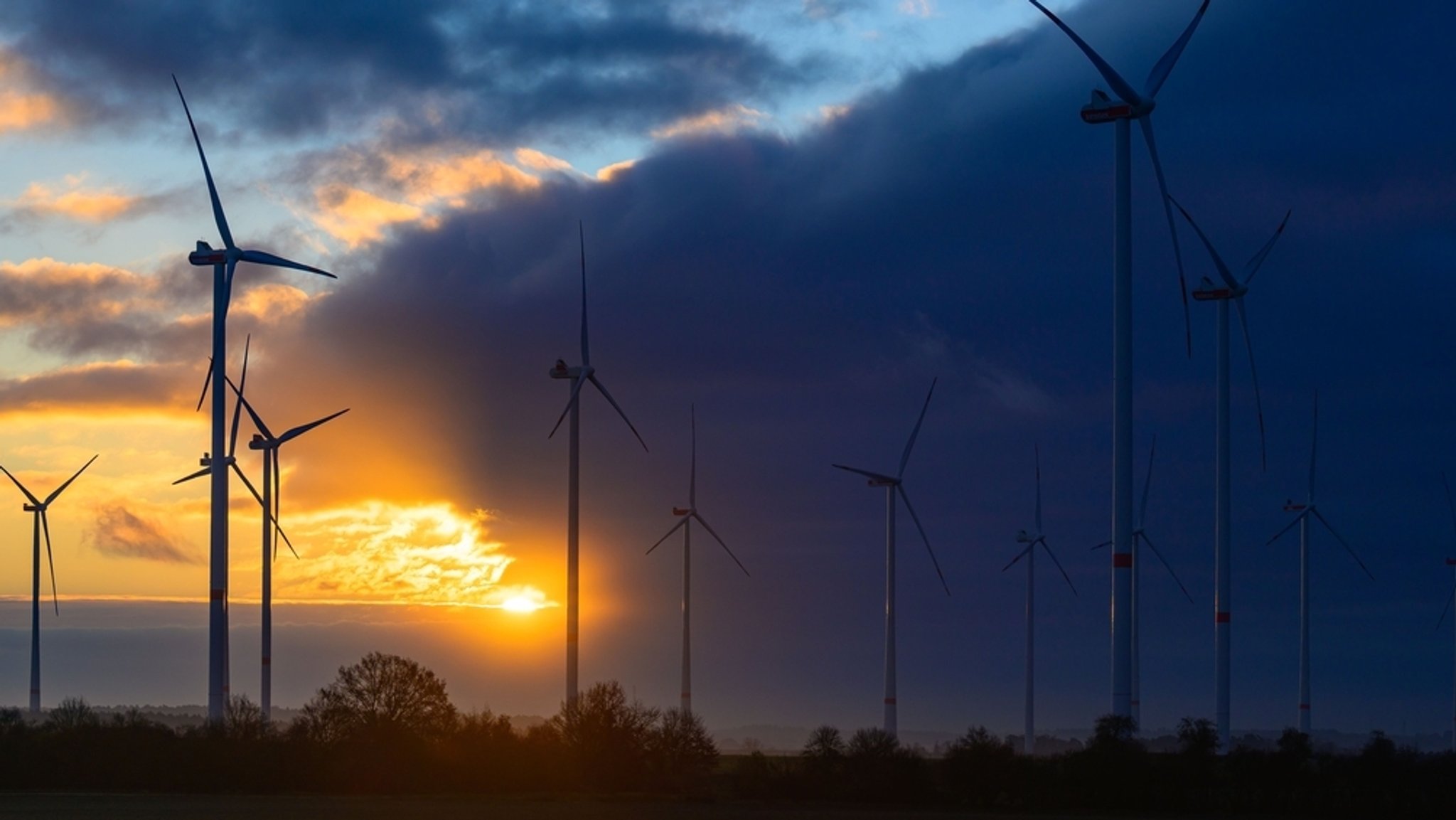 Windräder bei Sonnenaufgang mit dunklen Wolken (Symbolbild).