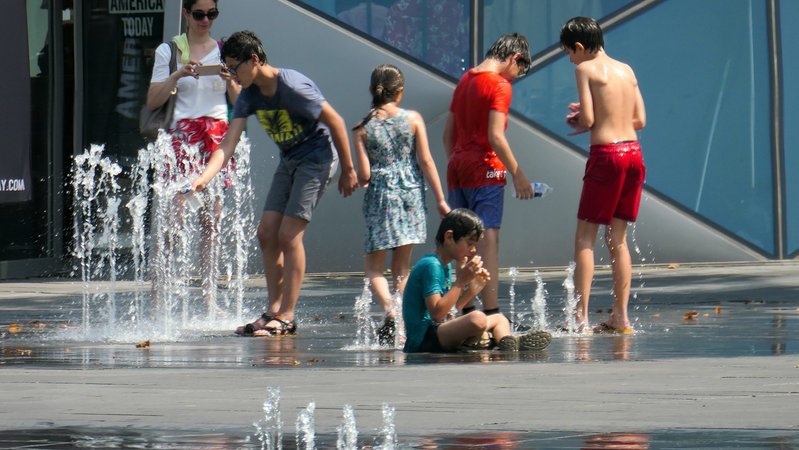 Menschen kühlen sich im Sommer an einem Springbrunnen ab.