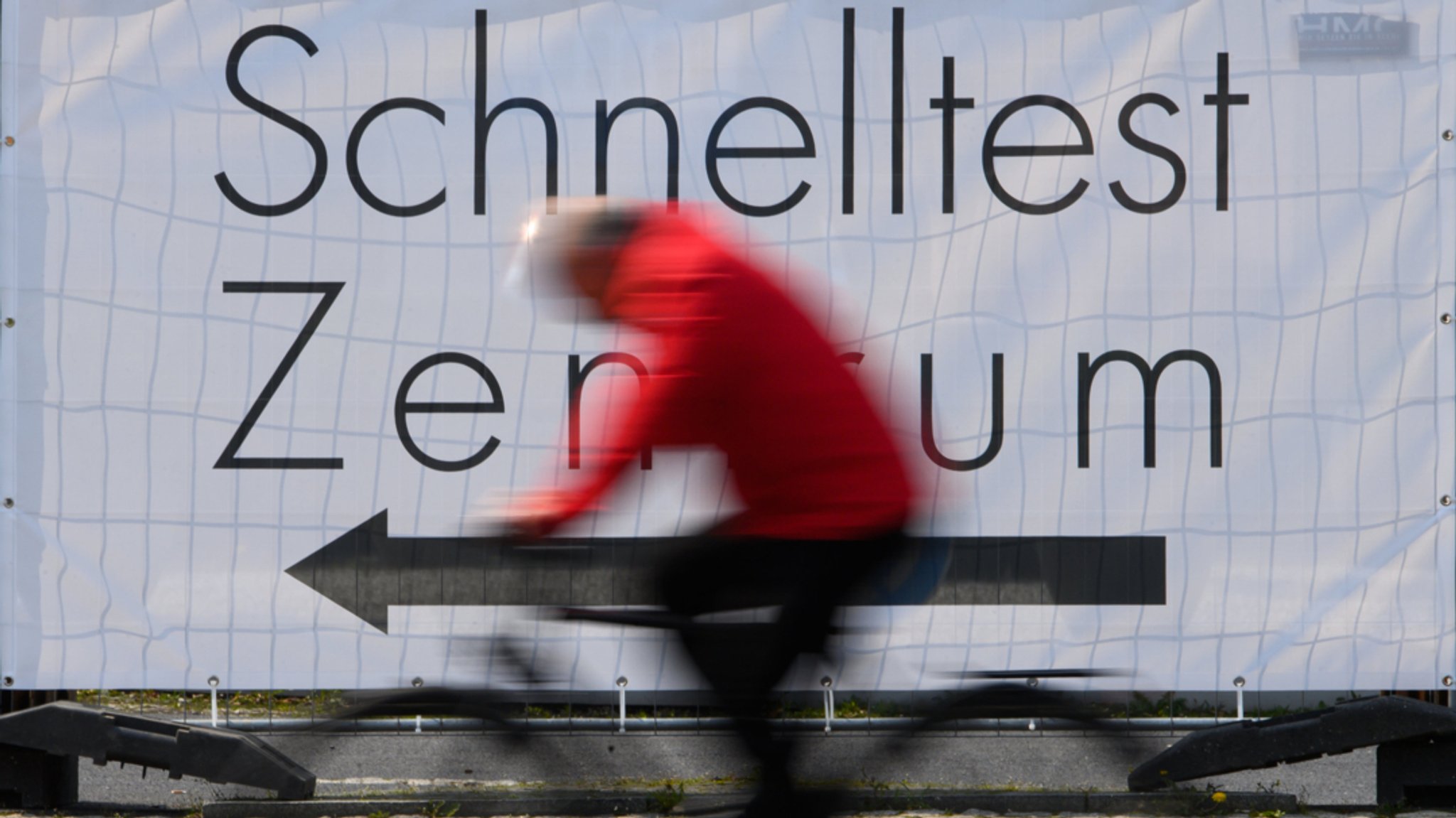 Eine Fahrradfahrer fährt an einem Banner mit der Aufschrift "Schnelltest Zentrum" vorbei. 