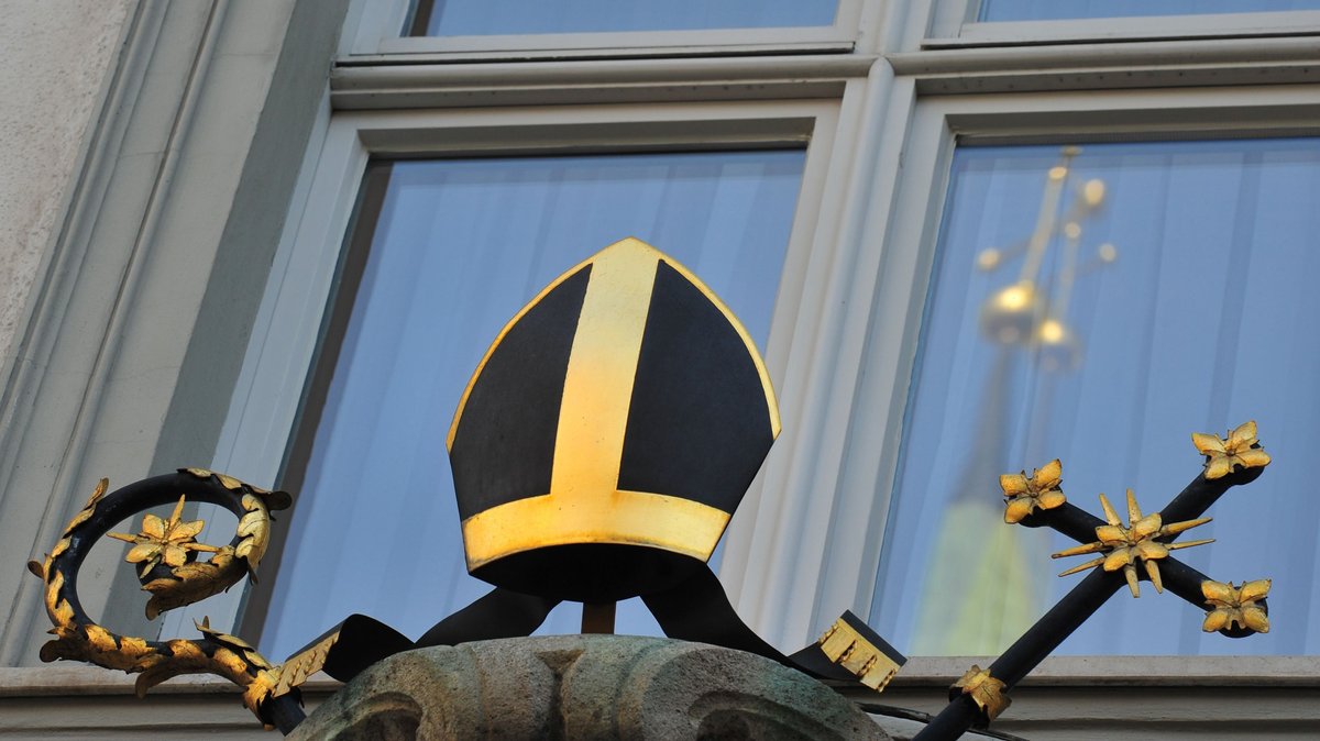 Das Kreuz des Doms spiegelt sich in einem Fenster am Augsburger Bischofspalais. 