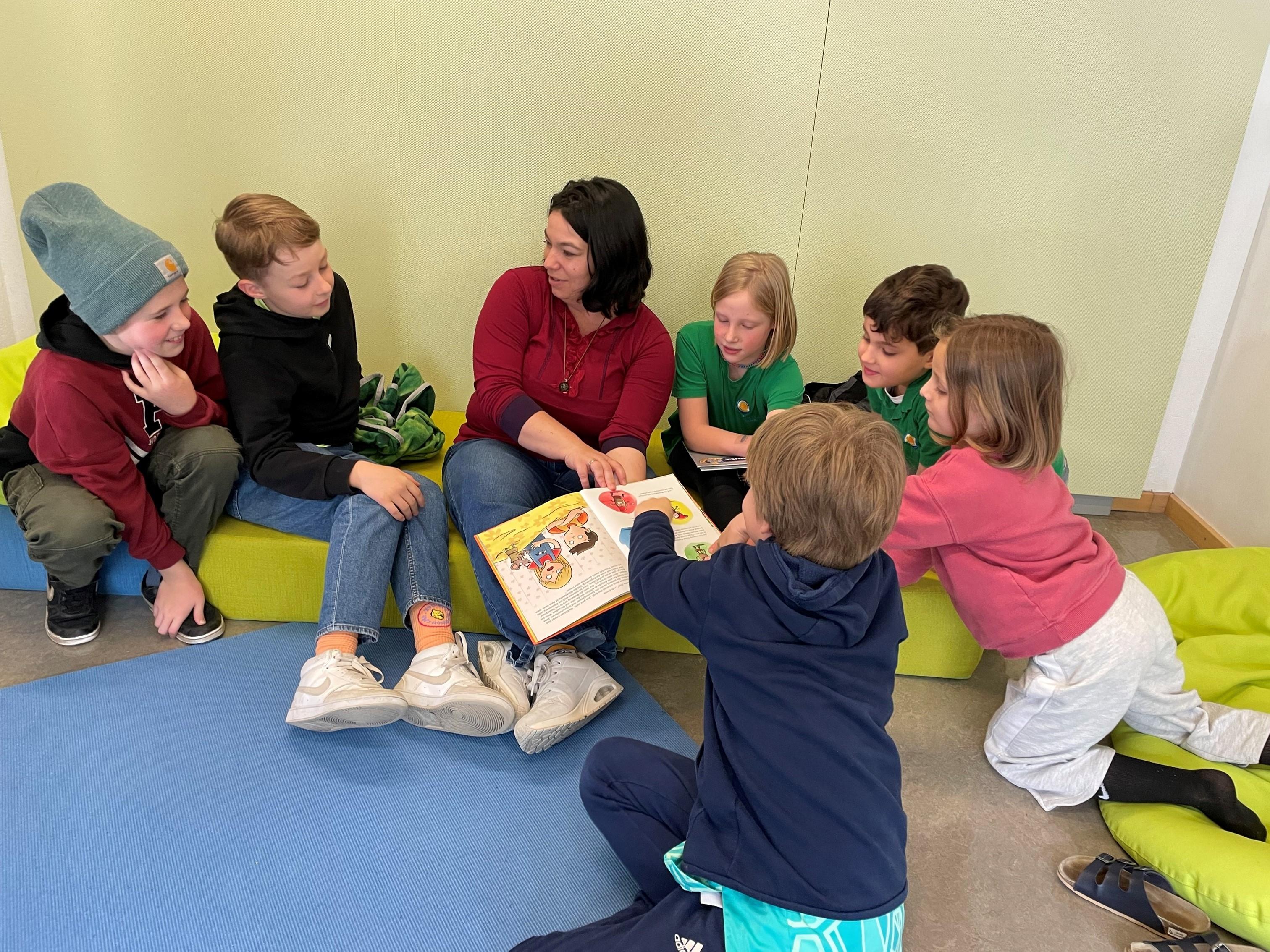 Eine Pädagogin mit einem Buch ist umringt von Grundschulkindern. 