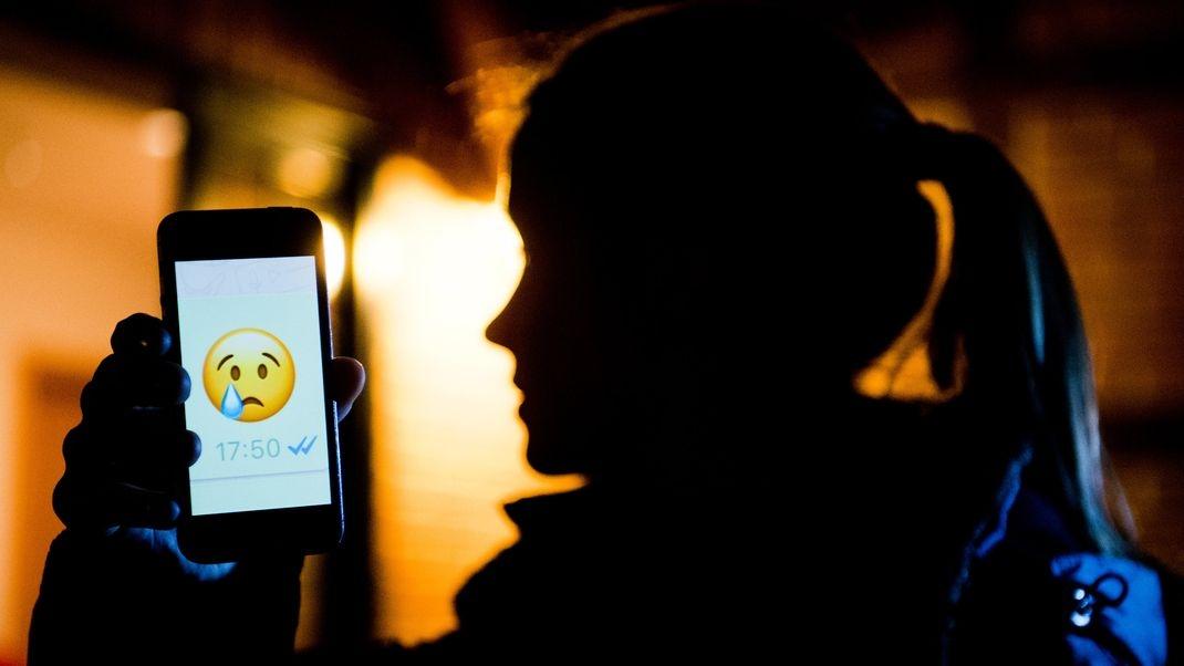 Ein junges Mädchen zeigt das Display eines Smartphones mit einem weinenden Emoji bem Messenger «WhatsApp» (gestellte Szene).