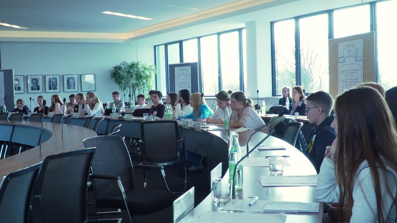 Im Landratsamt Mühldorf sitzen Schülerinnen und Schüler an halbrunden Tischen und spielen ein politisches Planspiel. | Bild: BR / Katharina Narr Im Landratsamt Mühldorf sitzen Schülerinnen und Schüler an halbrunden Tischen und spielen ein politisches Planspiel.