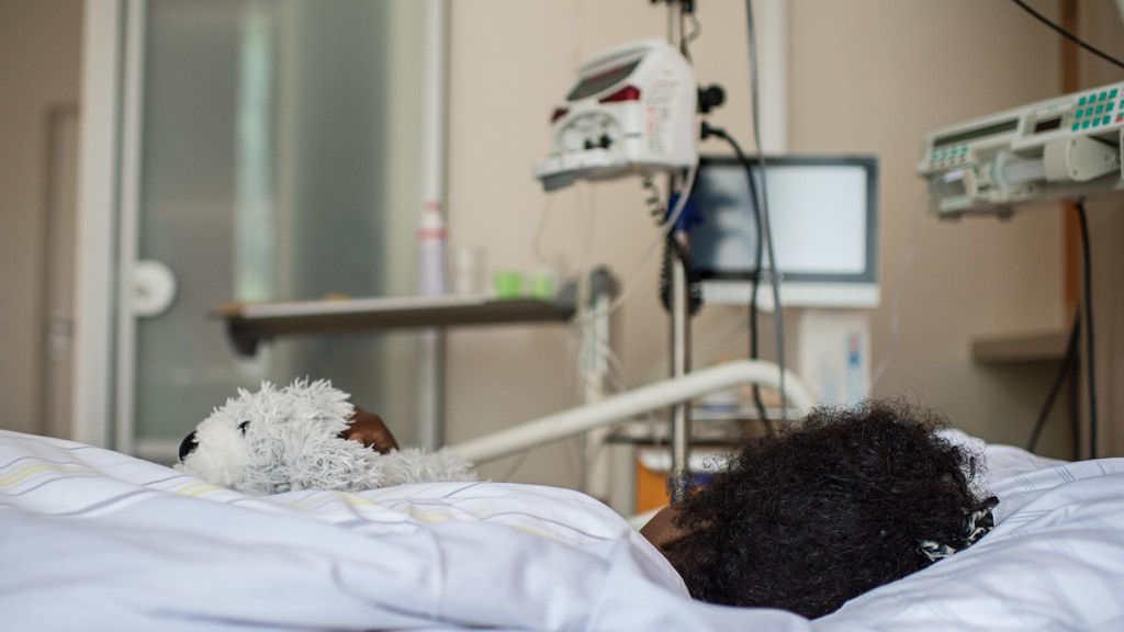 Kind liegt mit Stofftier in einem Krankenhausbett