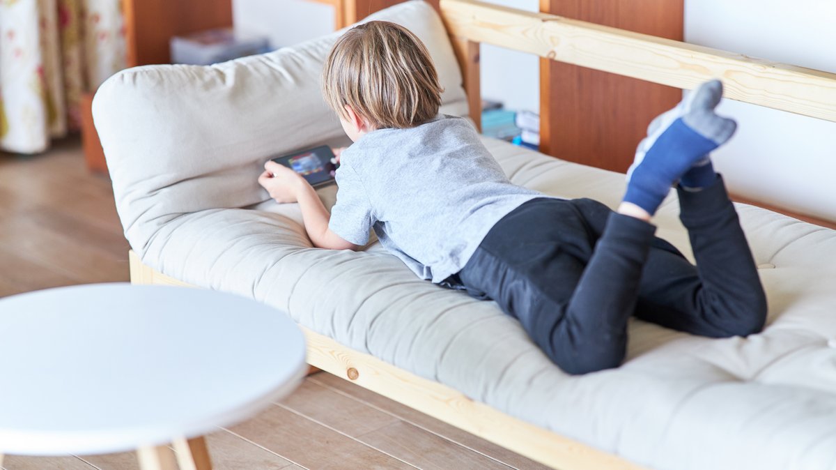 Junge liegt auf der Couch und spielt ein Videospiel auf dem Smartphone (Symbol- und Archivbild)