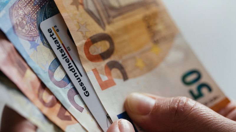 Eine Krankenkassen-Chipkarte zwischen Geldscheinen | Bild: BR/Julia Müller Eine Krankenkassen-Chipkarte zwischen Geldscheinen