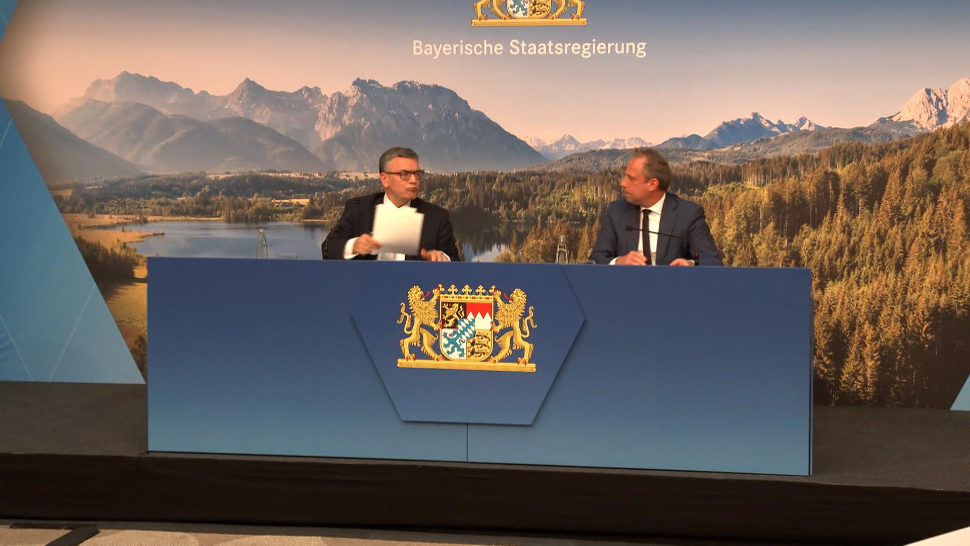 Zwei Männer sitzen hinter einem blauen Pult bei einer Pressekonferenz.