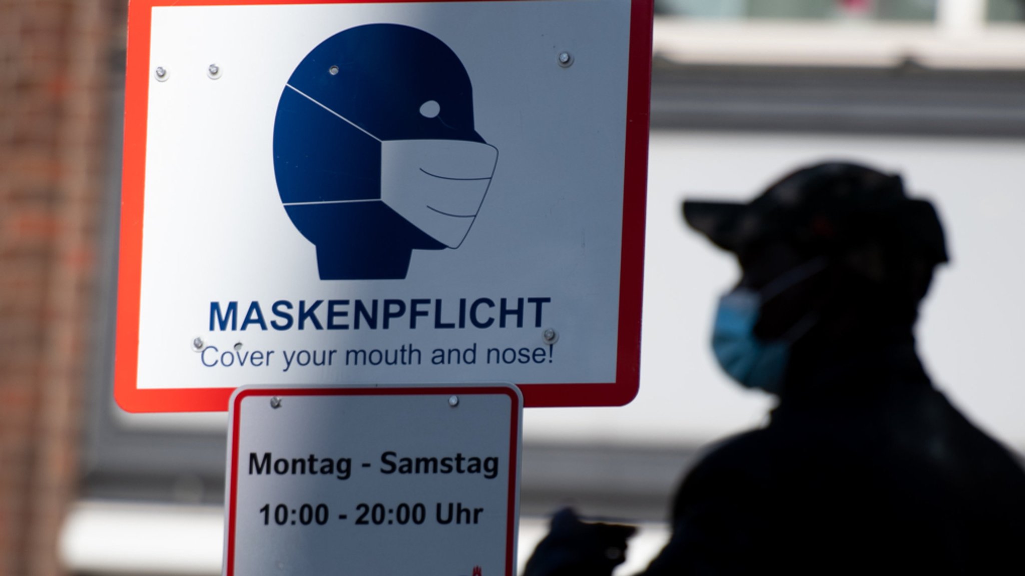 in Mann geht in der Innenstadt an einem Schild mit der Aufschrift "Maskenpflicht" vorbei.