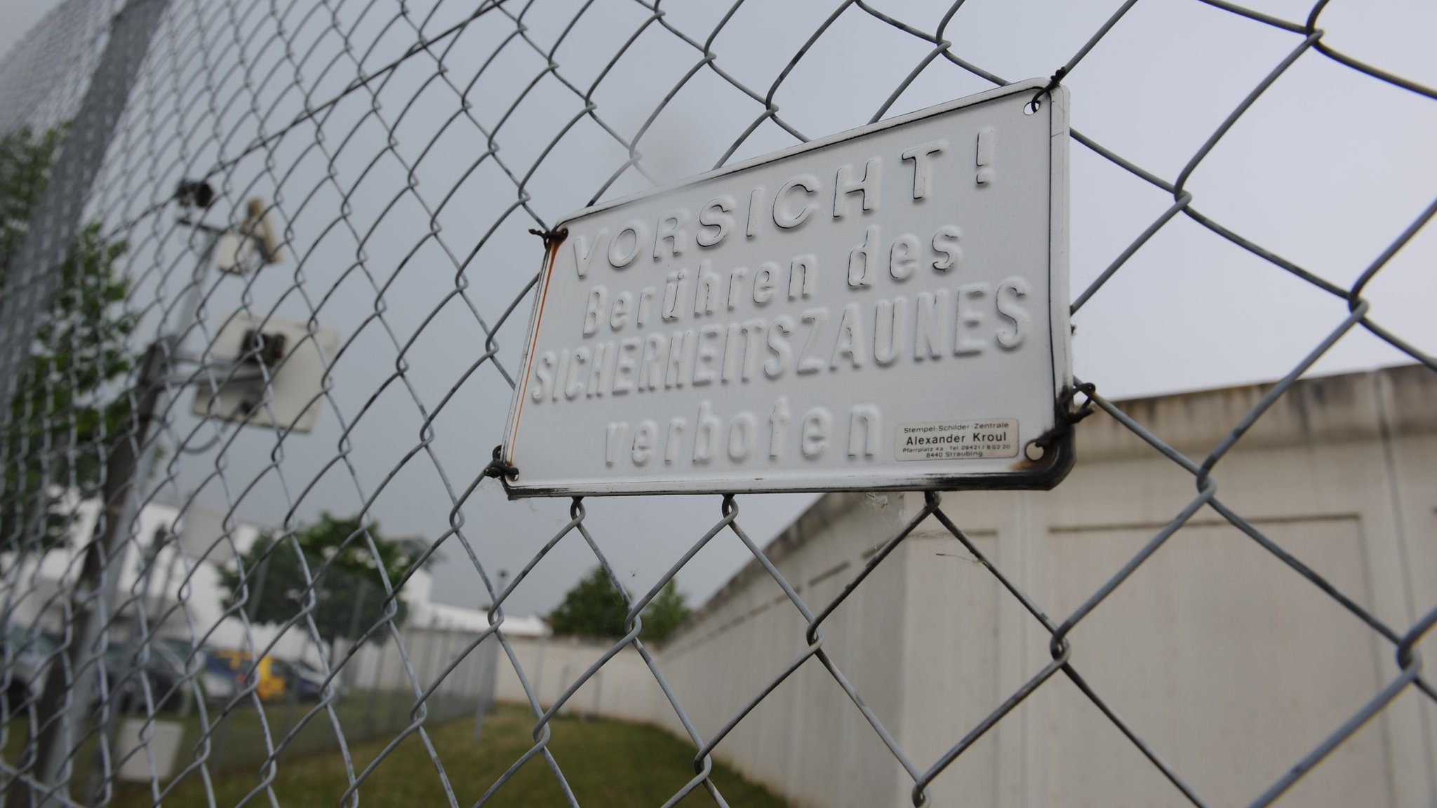 Ein Schild mit der Aufschrift "Vorsicht! Berühren des Sicherheitszaunes verboten" ist am Zaun vor der Mauer der Forensisch-Psychiatrischen Klinik in Straubing angebracht