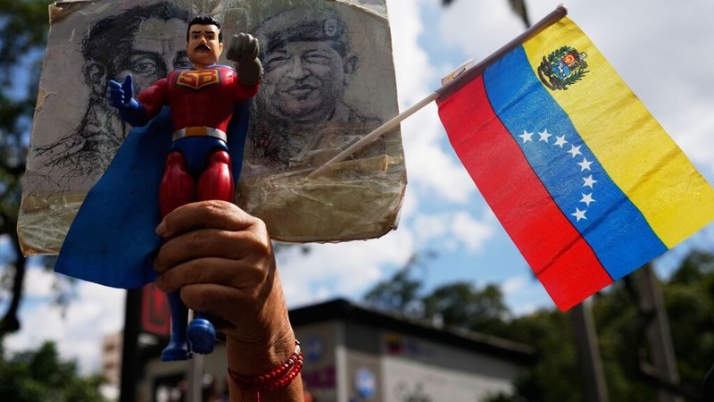 04.01.2026, Venezuela, Caracas: Ein Anhänger der Regierung hält eine Action-Figur von Super Bigote während einer Demonstration, bei der die Freilassung von Präsident Nicolas Maduro gefordert wird, nachdem die US-Streitkräfte ihn gefangen genommen und in die Vereinigten Staaten geflogen haben. Foto: Ariana Cubillos/AP/dpa +++ dpa-Bildfunk +++ | Bild: dpa-Bildfunk/Ariana Cubillos 04.01.2026, Venezuela, Caracas: Ein Anhänger der Regierung hält eine Action-Figur von Super Bigote während einer Demonstration, bei der die Freilassung von Präsident Nicolas Maduro gefordert wird, nachdem die US-Streitkräfte ihn gefangen genommen und in die Vereinigten Staaten geflogen haben. Foto: Ariana Cubillos/AP/dpa +++ dpa-Bildfunk +++